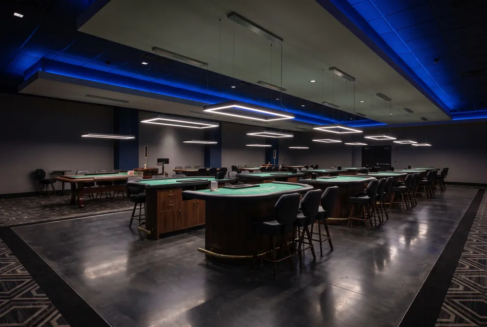 Generated image: rows of empty green-felt table games under square pendant lamps and blue ceiling light; not a photograph of the casino.